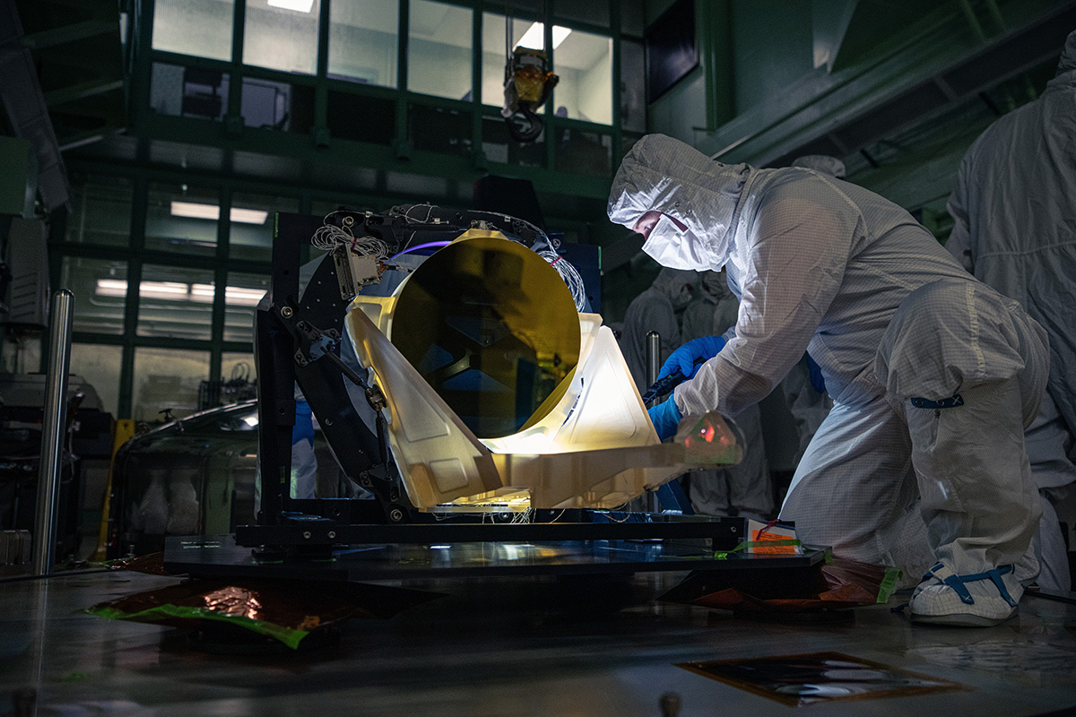 A technician in a darkened clean room inspects a prototype telescope for the LISA gravitational-wave mission