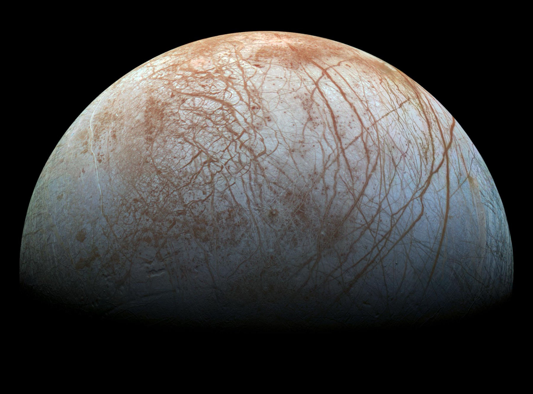 Jupiter's moon Europa, one of the best places to look for life in the universe, its icy surface crossed by long reddish brown cracks and ridges