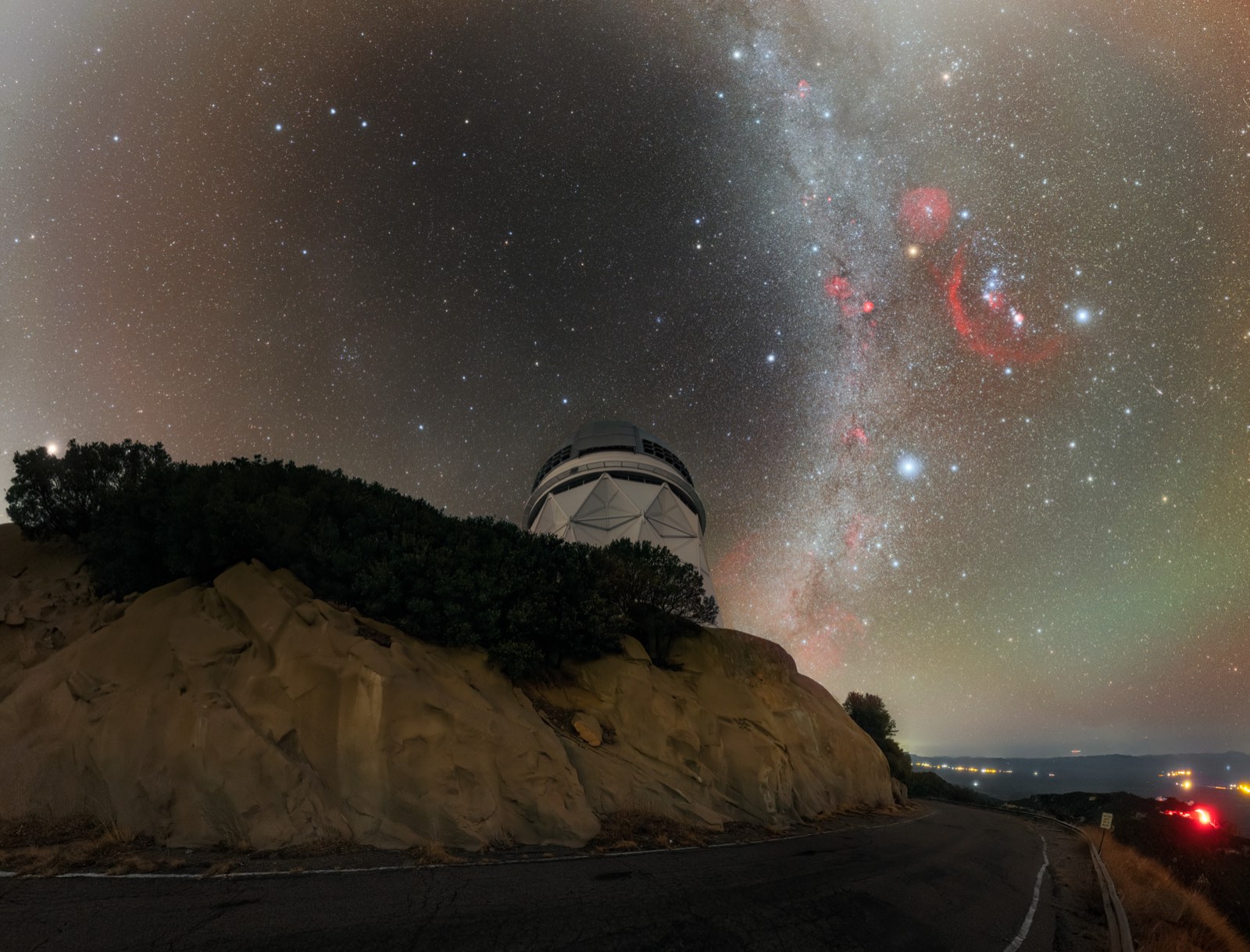 The dome of the Mayall 4-meter Telescope at Kitt Peak National Observatory on a rocky ridge under the Milky Way at night