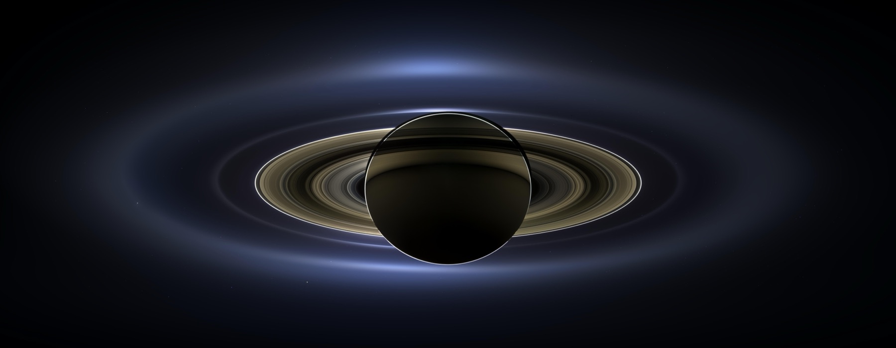 Cassini view of Saturn backlit by the Sun, its rings glowing in a wide halo against dark space, a reminder of how the solar system formed from a flat disk