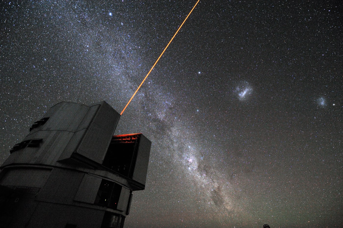 An orange laser beam shoots from a Very Large Telescope unit at Paranal, one of the great ground observatories alongside the space telescopes, into a night sky crossed by the Milky Way